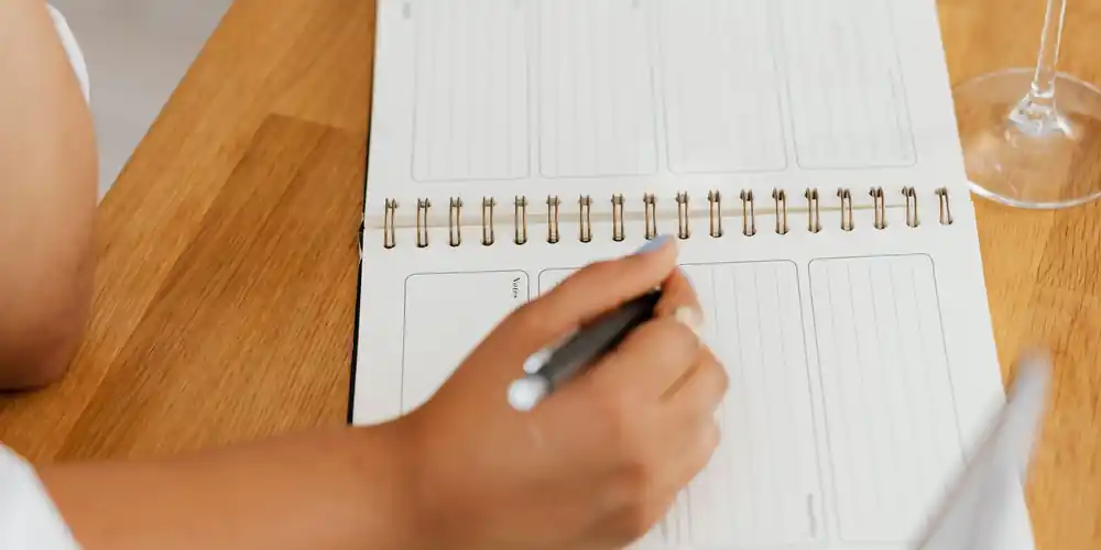 Writing a schedule in a planner next to a laptop